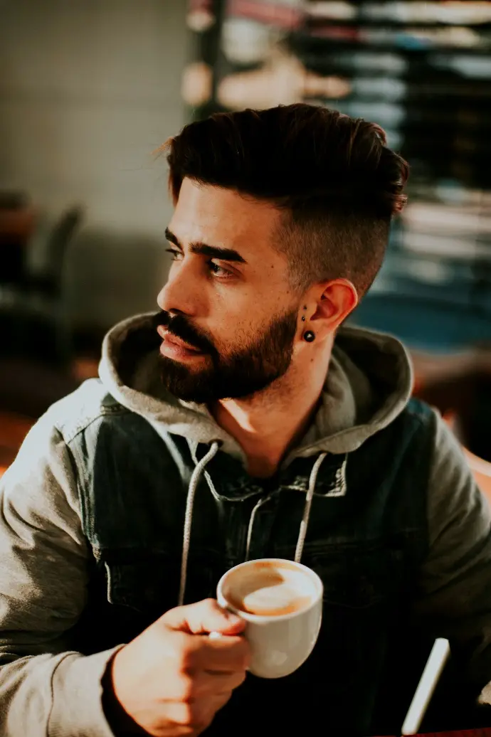 shallow focus photo of man in hoodie holding white ceramic mug